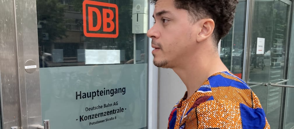 Una persona con un sobre, delante de la entrada de la sede principal de la empresa Deutsche Bahn DB