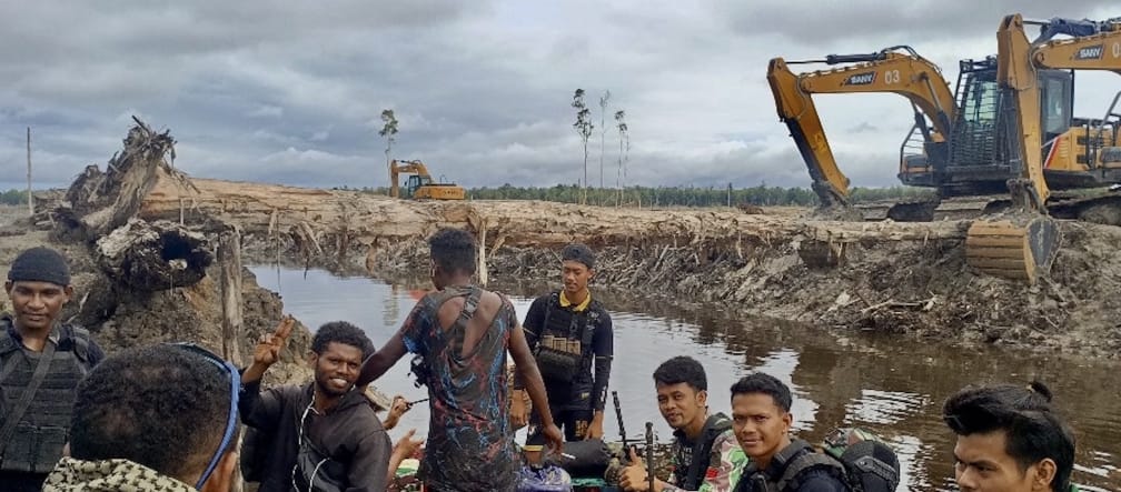 Grupo de hombres con excavadoras mecánicas al fondo frente a un paisaje devastado