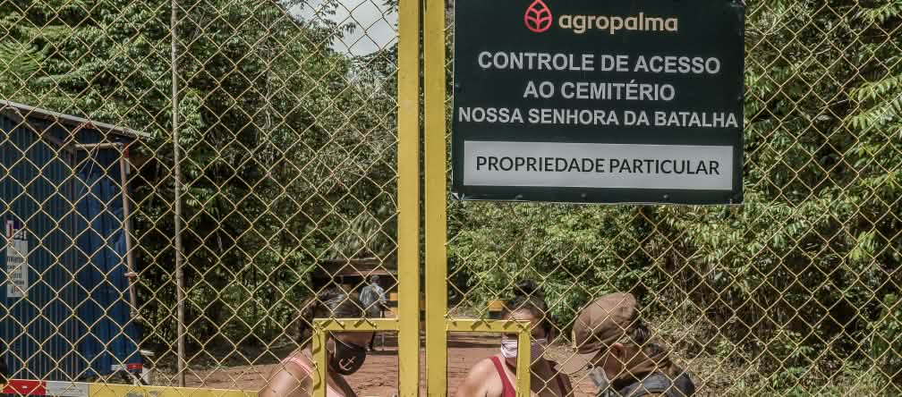 Para acudir al cementerio comunitario, dos mujeres se ven obligadas a pasar por un punto de control de la empresa Agropalma. En el cartel de la empresa se lee: “Agropalma. Control de acceso al cementerio de Nossa Senhora da Batalha. Propiedad privada"
