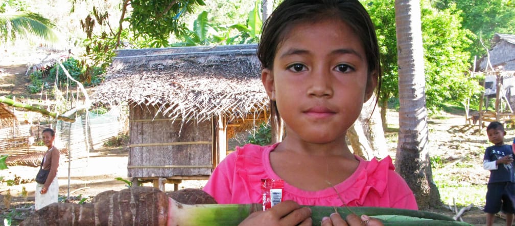 Niña Pala’wan en su comunidad con un taro, verdura local