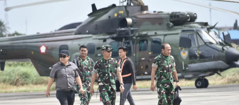 Tres soldados y dos civiles delante de un helicóptero