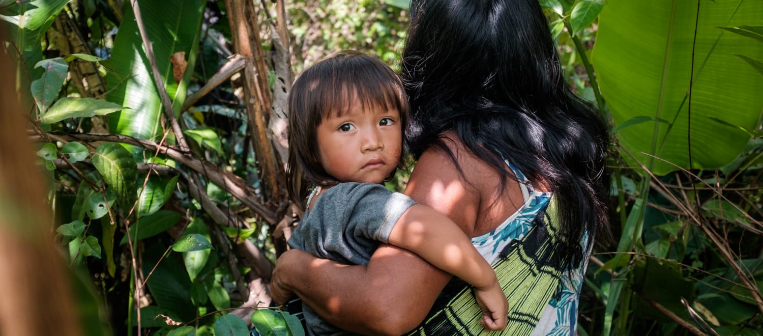 Mujer indígena ka'apor entre la vegetación de la selva amazónica con su hijo en brazos