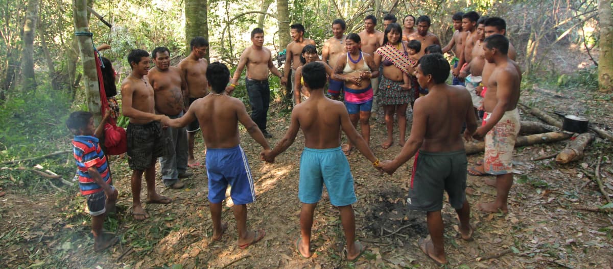 Indígenas ka'apor - niños, mujeres y hombres- situados entre los árboles, unen sus manos y forman un círculo