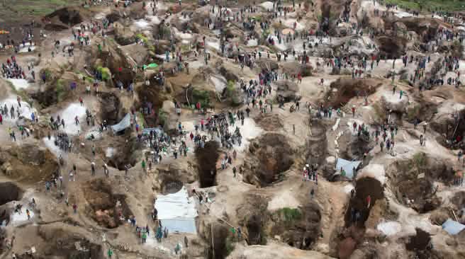 Vista aérea de una mina, con agujeros profundos, parcialmente llenos de agua, entre los cuales se encuentran numerosas personas