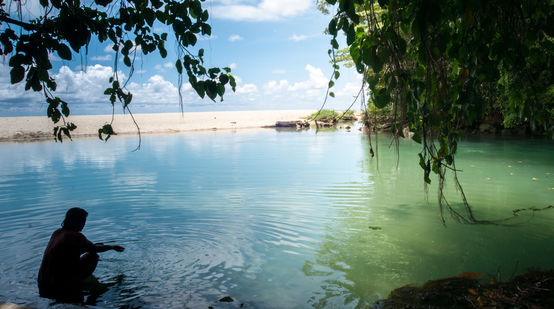 Una mujer en el agua en una bahía rodeada de rocas y arena