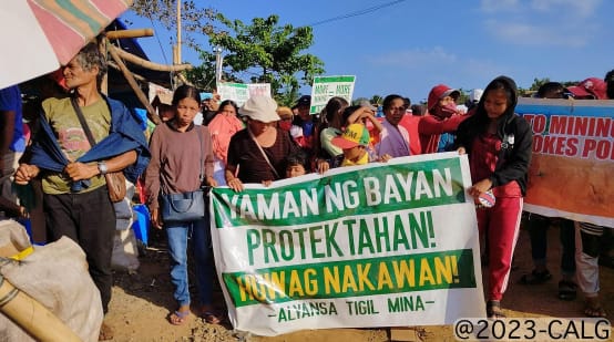 Un grupo de personas sostiene una pancarta en la que se lee (traducido): "¡Protejan la riqueza del pueblo! ¡No al saqueo! Alianza contra la Minería"