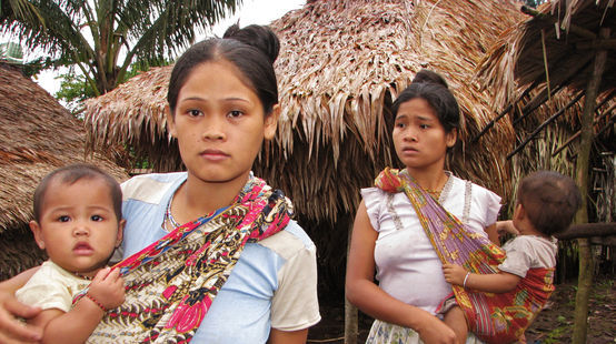 Dos mujeres con sus bebés frente a las casas de su comunidad