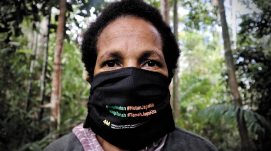 Mujer papú con tapabocas en el que se lee "Protege el bosque - el bosque nos protege"