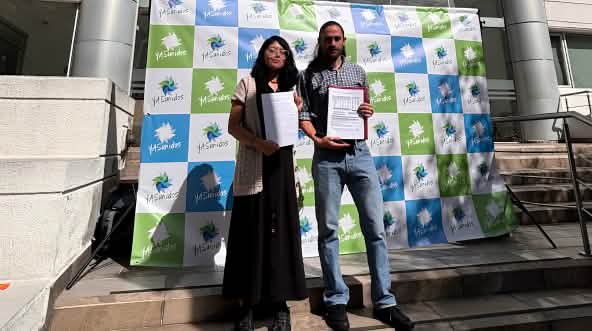 Una mujer y un hombre frente a un fotocall del colectivo YASunidos, delante de un edificio con documentos en la mano