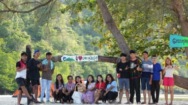 Un grupo de jóvenes de la organización Mother Nature Camboya sentados y de pie frente a un árbol en la playa