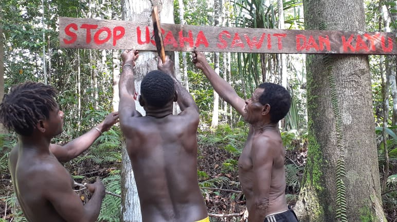 Tres indígenas papúes con un cartel en defensa de su bosque