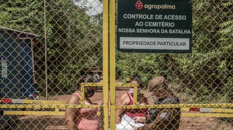 Para acudir al cementerio comunitario, dos mujeres se ven obligadas a pasar por un punto de control de la empresa Agropalma. En el cartel de la empresa se lee: “Agropalma. Control de acceso al cementerio de Nossa Senhora da Batalha. Propiedad privada"