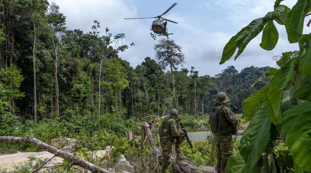 Dos agentes armados de la agencia ambiental IBAMA, vestidos con trajes de camuflaje, bajo un helicóptero durante en una operación de contra la minería ilegal de oro en la selva tropical amazónica