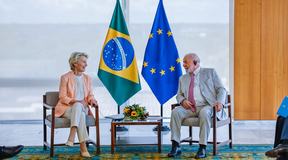 Presidente de Brasil, Lula da Silva y presidenta de la Comisión Europea, Ursula von der Leyen sentados, mirándose, delante de dos banderas, una de Brasil y la otra de la Unión Europea