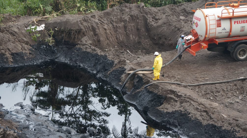 Dos trabajadores petroleros succionan con manguera el crudo de una balsa en tierra hacia un camión cisterna