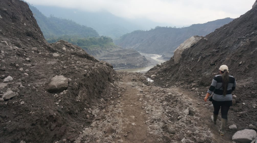 Una mujer camina por un carril entre dos terraplenes de tierra y rocas hacia el valle erosionado del río Coca, que se puede ver al fondo