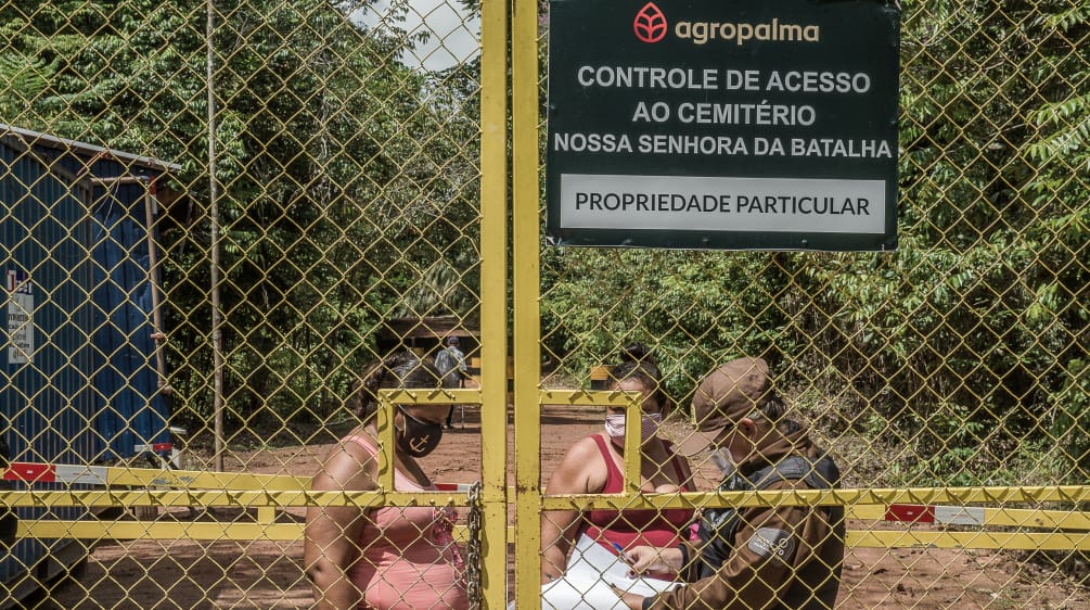 Para acudir al cementerio comunitario, dos mujeres se ven obligadas a pasar por un punto de control de la empresa Agropalma. En el cartel de la empresa se lee: “Agropalma. Control de acceso al cementerio de Nossa Senhora da Batalha. Propiedad privada"