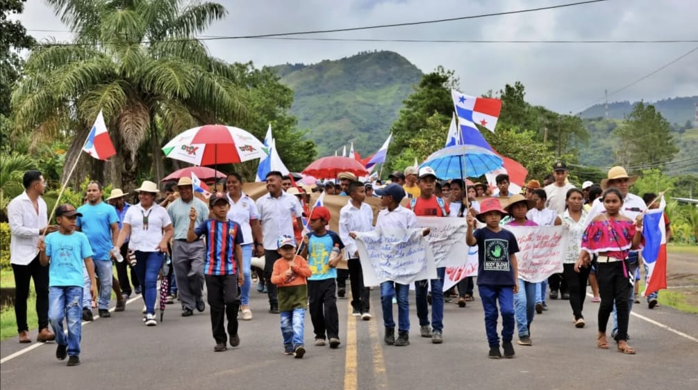 Manifestantes marchan con pancartas, banderas nacionales y paraguas por una carretera en Panamá