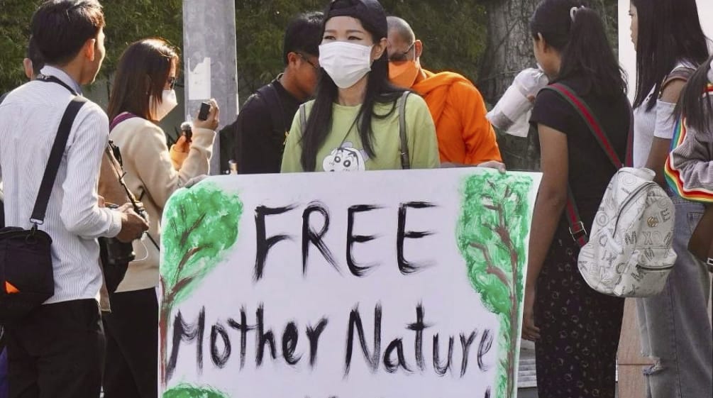 Joven mujer con un gran cartel en el que se lee «¡Liberad a los activistas de Mother Nature!».
