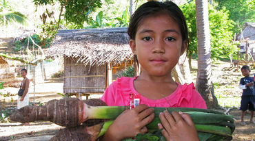 Niña Pala’wan en su comunidad con un taro, verdura local